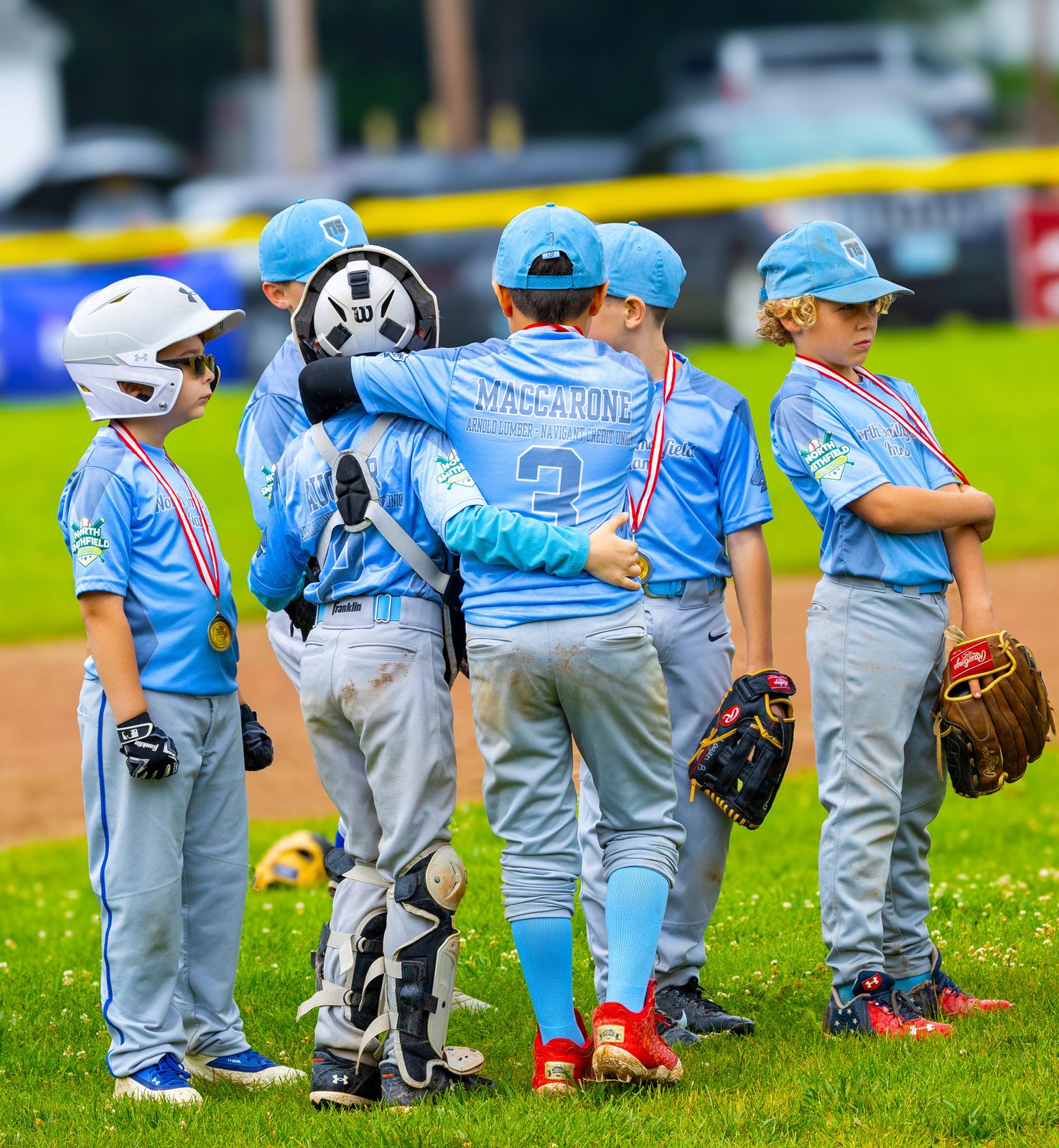 Youth baseball team in light blue uniforms and medals huddled together