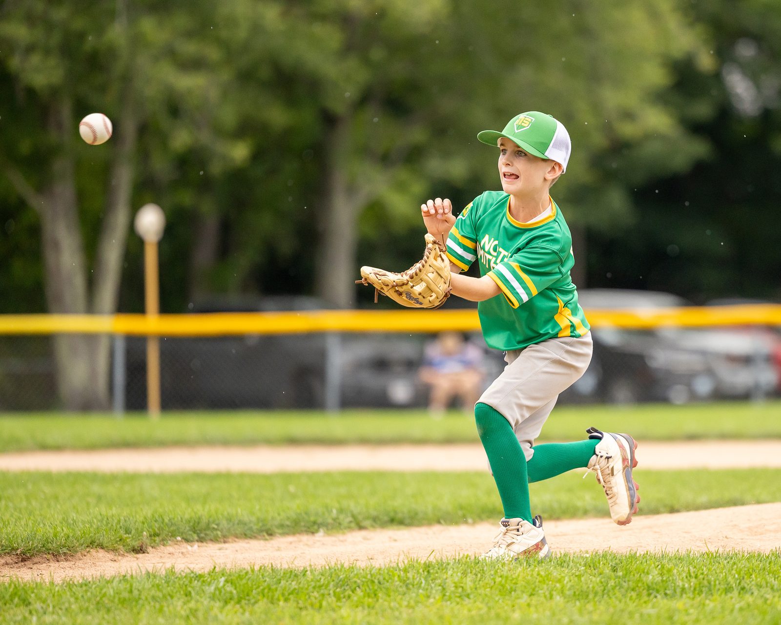 Young baseball player in a green uniform fielding a throw